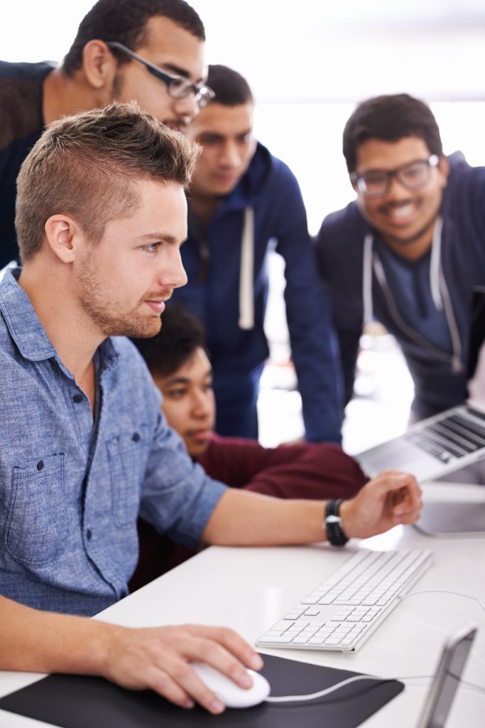 Cropped shot of young students gathered around a computer
